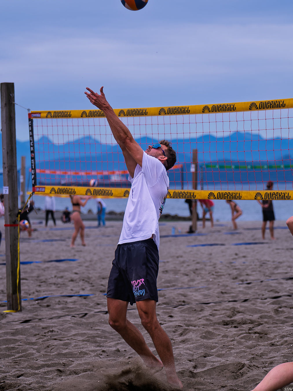 Player in NNS shorts setting the ball at Spanish Banks with the North Shore mountains behind